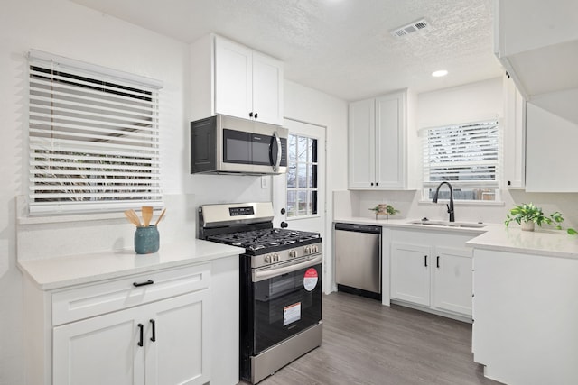 kitchen featuring stainless steel appliances, light countertops, light wood-style flooring, white cabinetry, and a sink