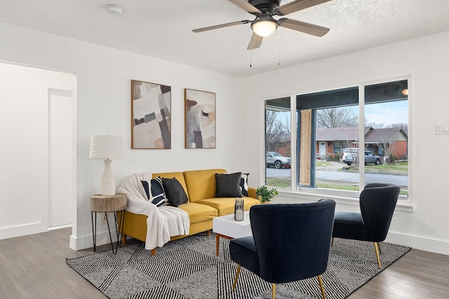 living area with a ceiling fan, baseboards, and wood finished floors