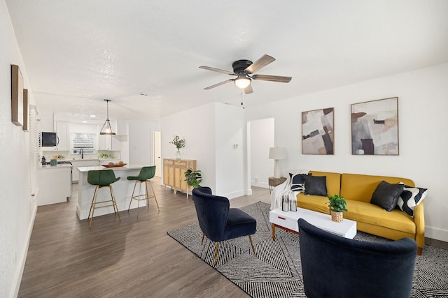 living area featuring a ceiling fan, dark wood finished floors, and baseboards