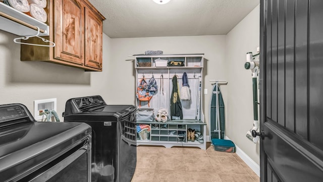 clothes washing area featuring a textured ceiling, light tile patterned floors, washing machine and dryer, baseboards, and cabinet space