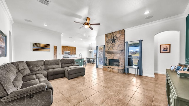 living room featuring light tile patterned flooring, a fireplace, a ceiling fan, visible vents, and crown molding