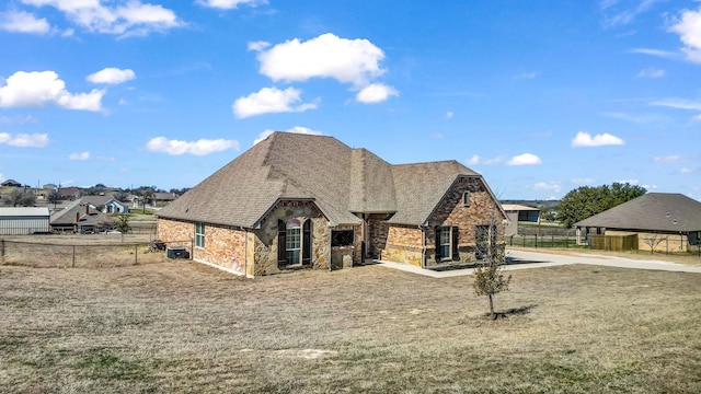 french country home featuring stone siding, fence, and roof with shingles