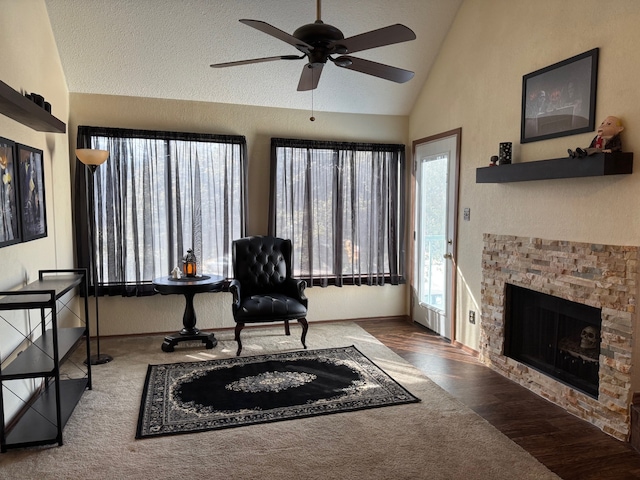 living area featuring dark wood finished floors, ceiling fan, vaulted ceiling, a textured ceiling, and a stone fireplace