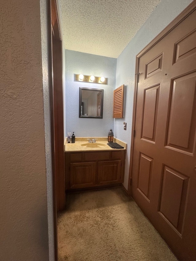 bathroom with a textured ceiling, a textured wall, carpet flooring, and vanity