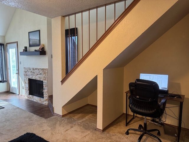 office space with light carpet, baseboards, a textured ceiling, and a stone fireplace