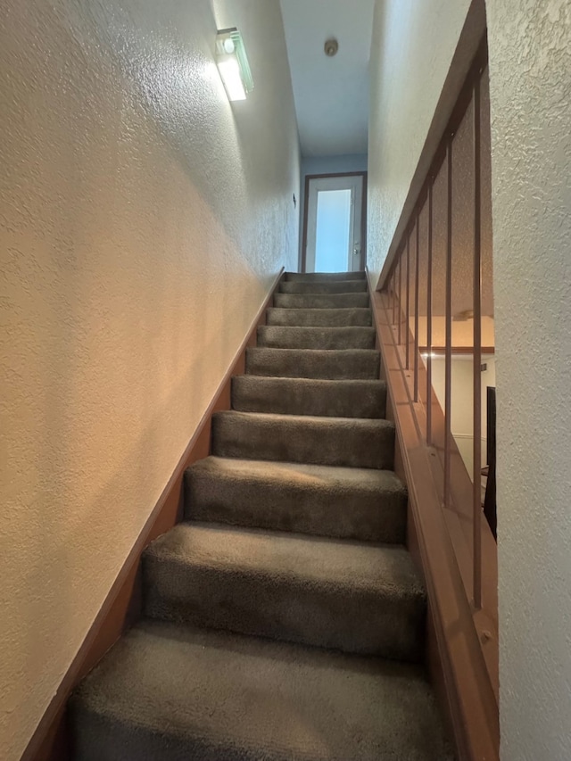 staircase featuring a textured wall and carpet