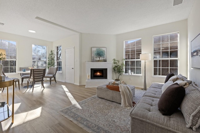 living room with visible vents, baseboards, a fireplace, wood finished floors, and a textured ceiling