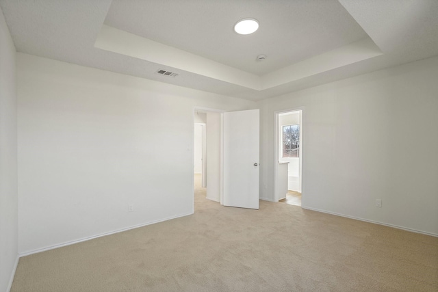 unfurnished room with a raised ceiling, visible vents, light carpet, and baseboards