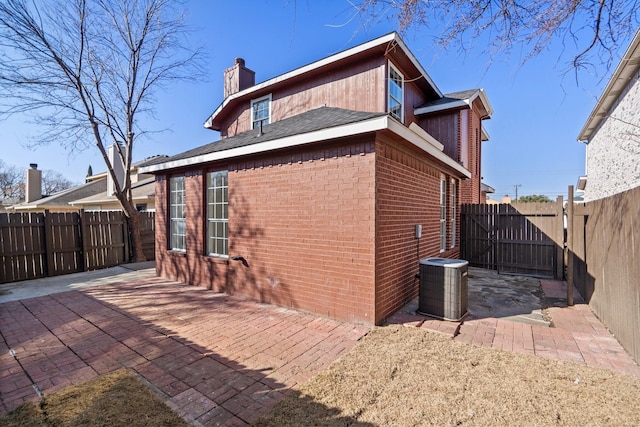 view of home's exterior featuring a fenced backyard, central AC unit, a patio, and brick siding