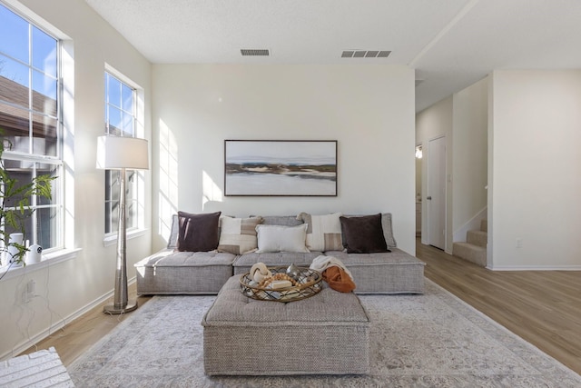 living area with visible vents, baseboards, wood finished floors, and stairway