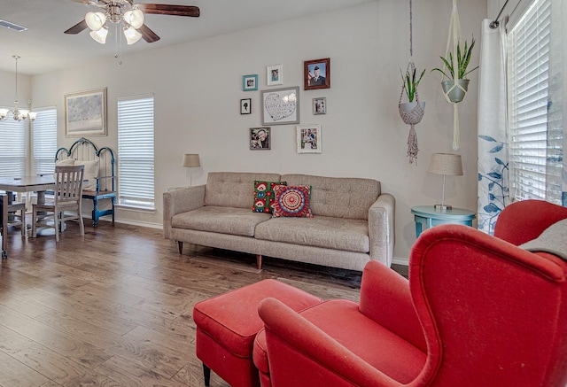 living room with visible vents, ceiling fan with notable chandelier, baseboards, and wood finished floors