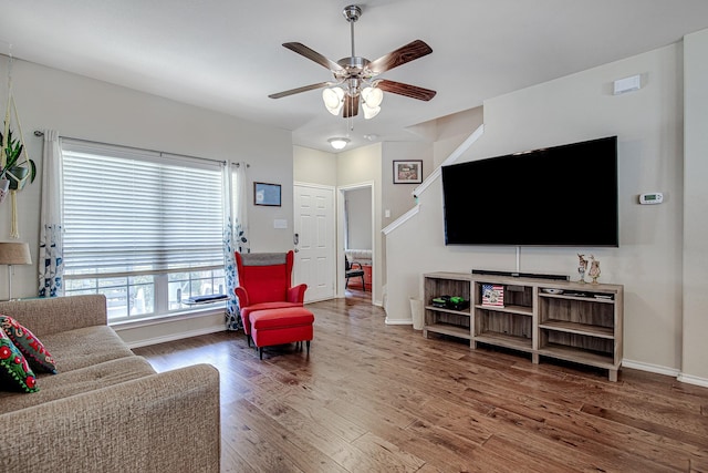 living room featuring stairway, baseboards, a ceiling fan, and wood finished floors