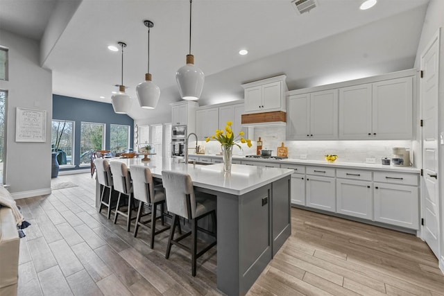 kitchen with pendant lighting, white cabinets, light countertops, and a center island with sink