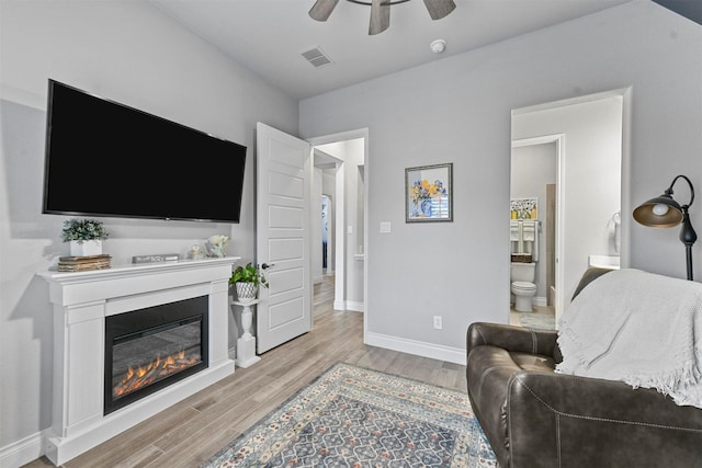 living area featuring light wood finished floors, visible vents, a ceiling fan, a glass covered fireplace, and baseboards