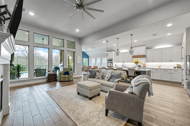 living room featuring a ceiling fan, recessed lighting, light wood-style flooring, and a high ceiling