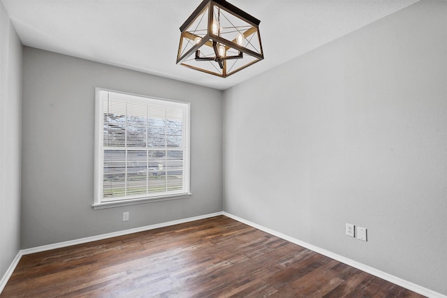 empty room with baseboards, dark wood finished floors, and a notable chandelier