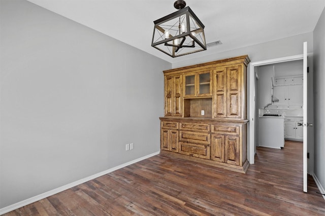 unfurnished dining area with an inviting chandelier, dark wood finished floors, visible vents, and baseboards