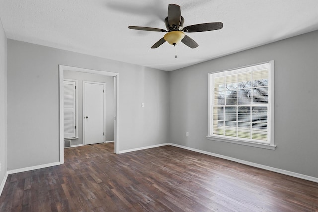 spare room featuring a textured ceiling, ceiling fan, dark wood-style flooring, and baseboards