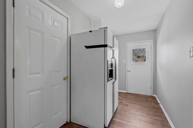 kitchen with light wood-type flooring, white refrigerator with ice dispenser, white cabinets, and baseboards