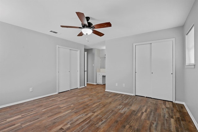 unfurnished bedroom with dark wood-style flooring, two closets, visible vents, and baseboards