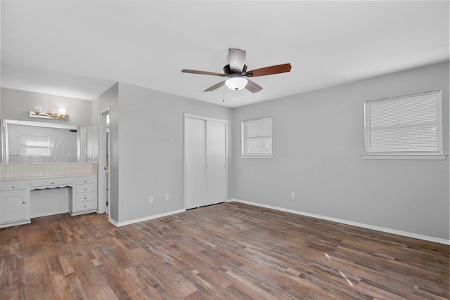 unfurnished bedroom with a ceiling fan, baseboards, a closet, dark wood-style floors, and ensuite bath