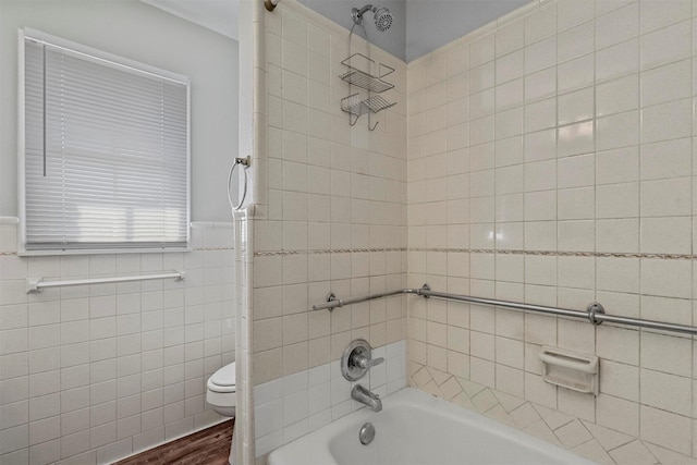 bathroom featuring a wainscoted wall, tile walls, shower / bathing tub combination, toilet, and wood finished floors