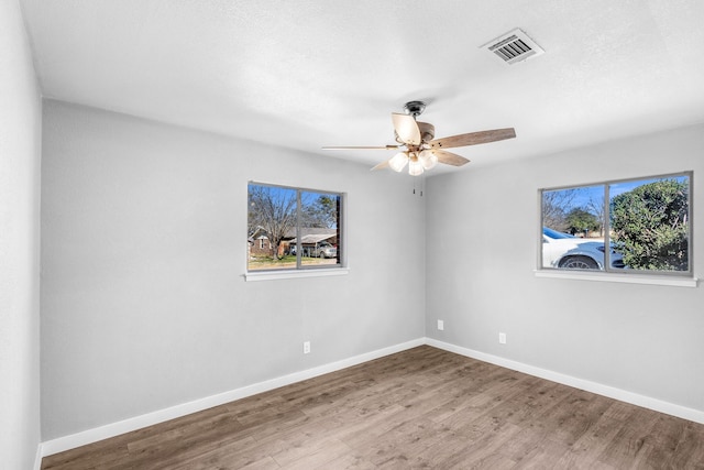 empty room featuring a healthy amount of sunlight, wood-type flooring, and ceiling fan