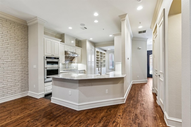 kitchen featuring kitchen peninsula, dark hardwood / wood-style flooring, brick wall, appliances with stainless steel finishes, and white cabinets