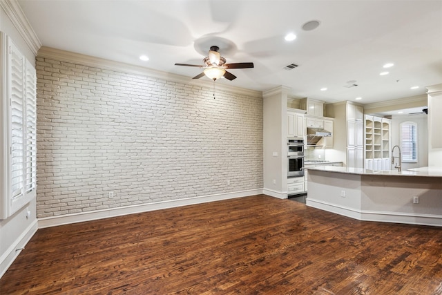 interior space with a breakfast bar area, dark wood-type flooring, brick wall, crown molding, and white cabinetry