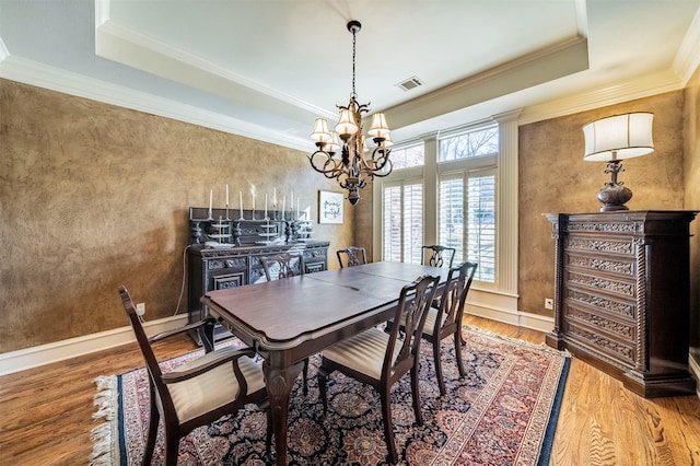 dining space with ornamental molding, a chandelier, wood-type flooring, and a raised ceiling