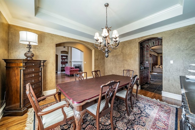 dining area with ornamental molding, a chandelier, a raised ceiling, and dark hardwood / wood-style floors