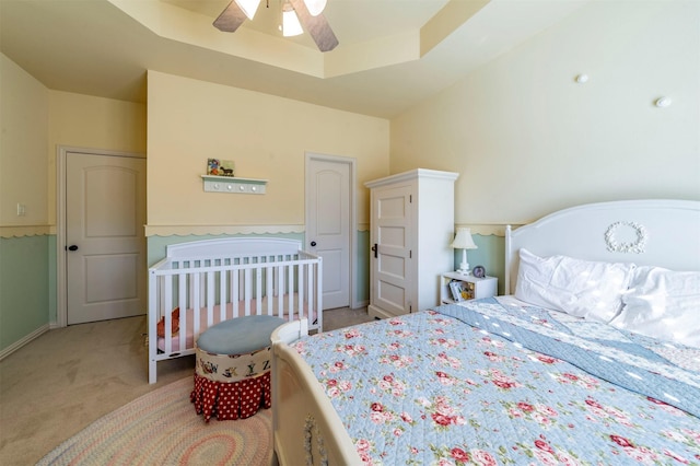 bedroom featuring ceiling fan, a tray ceiling, and light colored carpet