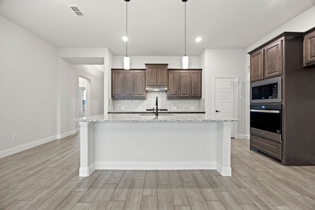 kitchen featuring built in microwave, oven, dark brown cabinetry, and light stone counters