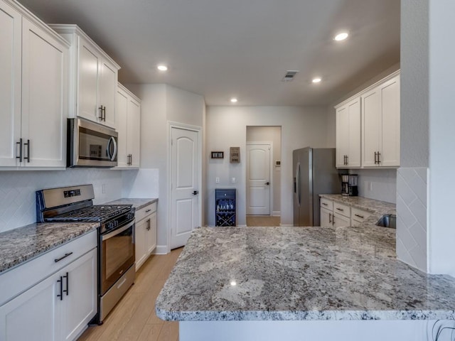 kitchen with visible vents, a peninsula, light wood-style flooring, appliances with stainless steel finishes, and white cabinetry