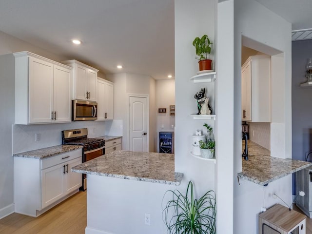 kitchen with light stone counters, stainless steel appliances, light wood-type flooring, and white cabinets