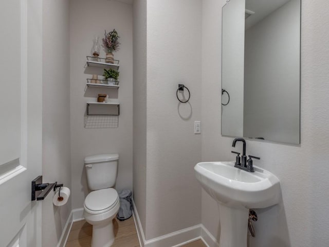 half bathroom with toilet, baseboards, and a sink