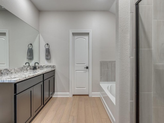 bathroom with vanity, wood finished floors, baseboards, a bath, and a shower with door