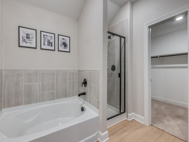 bathroom with a walk in closet, a stall shower, wood finished floors, baseboards, and a bath