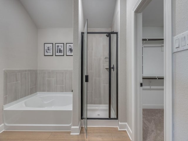 bathroom featuring wood finished floors, baseboards, a stall shower, a spacious closet, and a bath