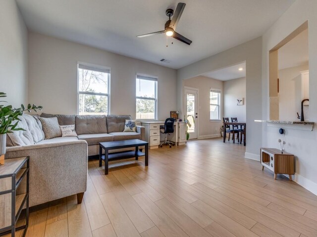 living room featuring light wood finished floors, visible vents, ceiling fan, and baseboards