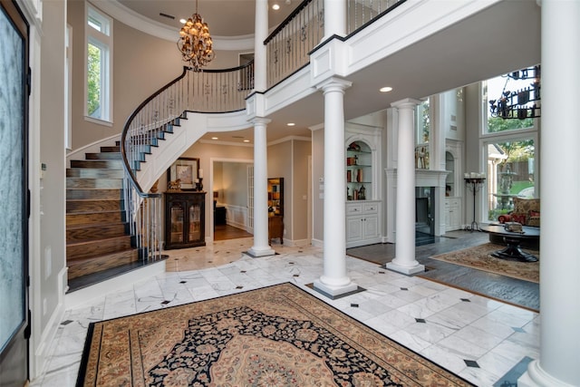 entryway featuring a wealth of natural light, crown molding, decorative columns, and a high ceiling