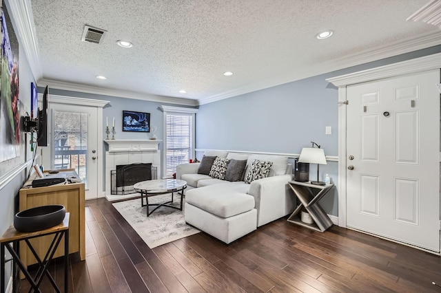 living room with a textured ceiling, dark wood-type flooring, a fireplace, visible vents, and ornamental molding