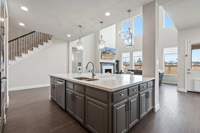 kitchen featuring light countertops, dark wood-type flooring, a sink, dishwasher, and a lit fireplace