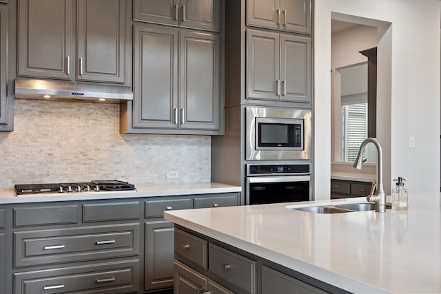 kitchen featuring appliances with stainless steel finishes, a sink, under cabinet range hood, and gray cabinetry