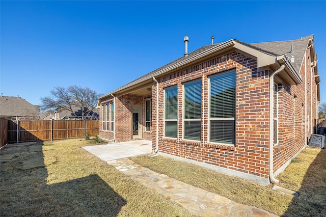 rear view of house featuring brick siding, a lawn, a patio area, and fence