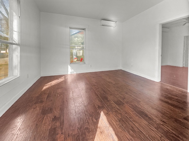 empty room featuring dark wood-style floors, an AC wall unit, and baseboards