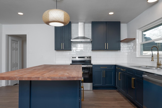 kitchen featuring appliances with stainless steel finishes, sink, pendant lighting, blue cabinets, and wall chimney range hood