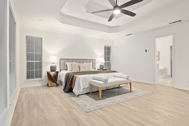 bedroom featuring ornamental molding, light hardwood / wood-style flooring, a raised ceiling, and ensuite bath