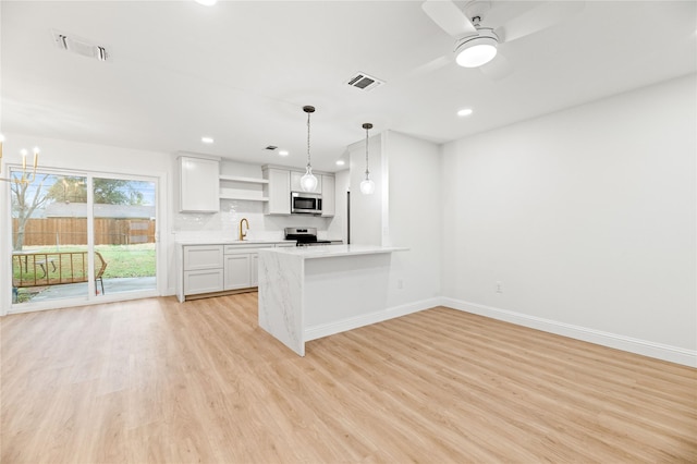 kitchen with appliances with stainless steel finishes, light countertops, hanging light fixtures, white cabinets, and open shelves