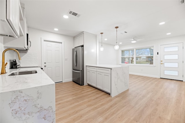 kitchen featuring a sink, freestanding refrigerator, visible vents, decorative light fixtures, and light stone countertops